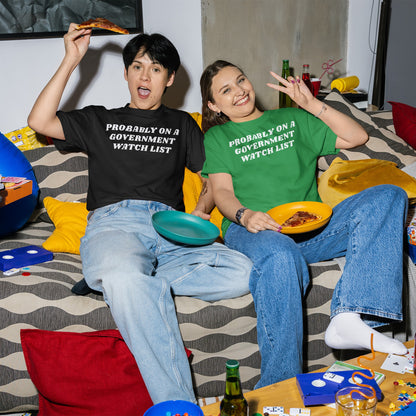 Two young adults wear Watch List T-shirt while lounging on a sofa. The scene, filled with pizza and board-game pieces, reflects a playful, defiant spirit against surveillance.