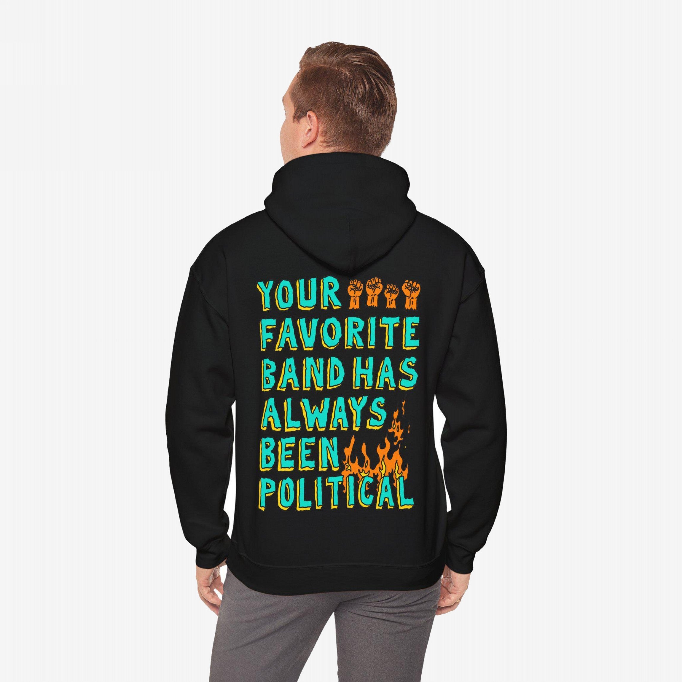 A person wears a black hoodie featuring the bold message YOUR FAVORITE BAND HAS ALWAYS BEEN POLITICAL with raised fists and flames, embodying rebellion and activism.